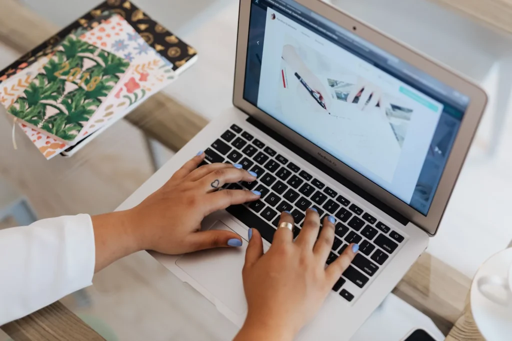 Kobieta pisze na laptopie przy biurku, obok notatniki