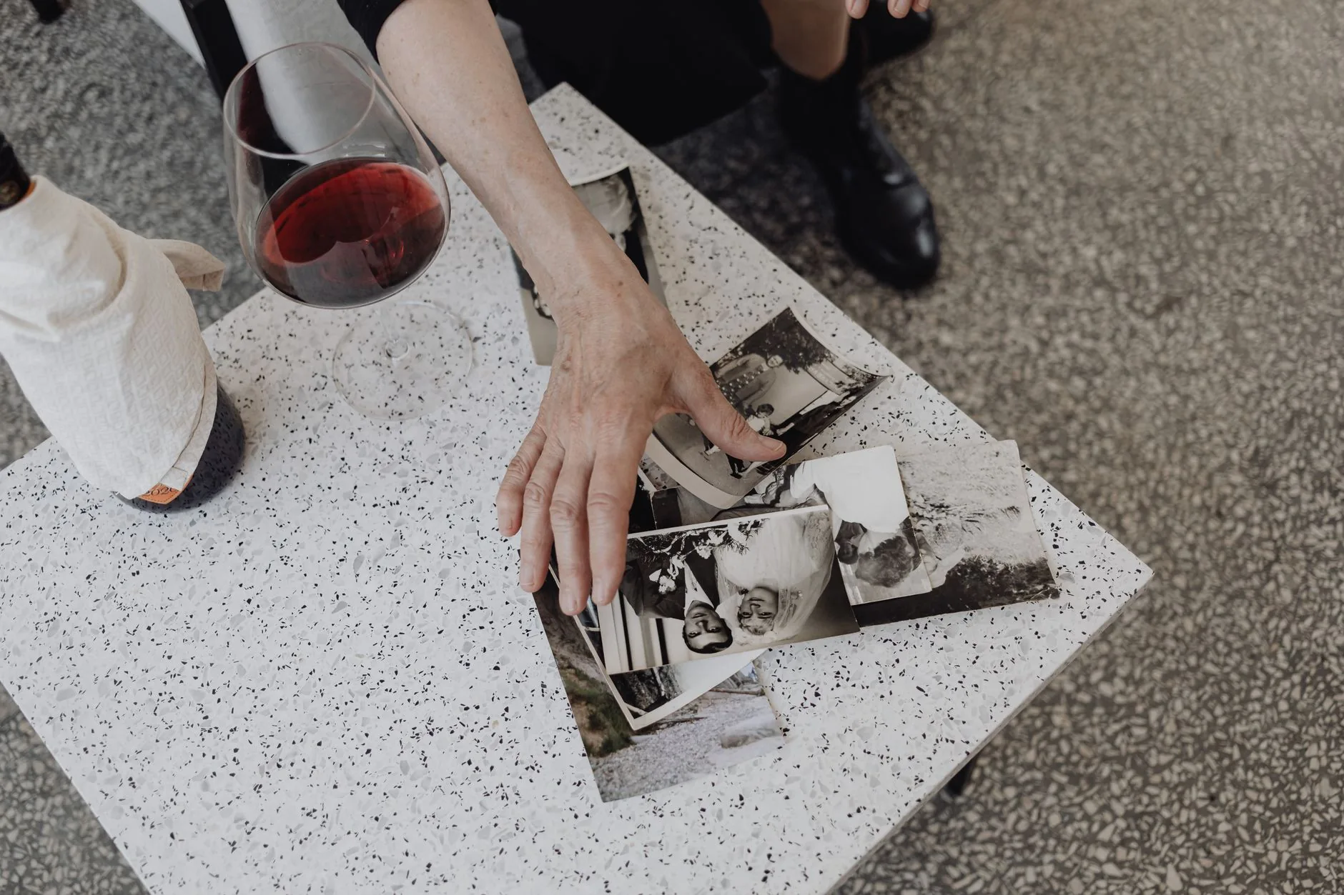 Na stole leżą stare fotografie, kieliszek wina i butelka