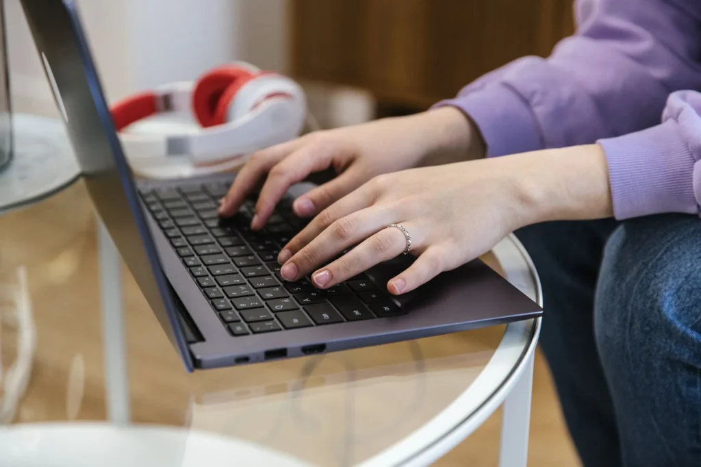Osoba pisze na laptopie, obok słuchawki
