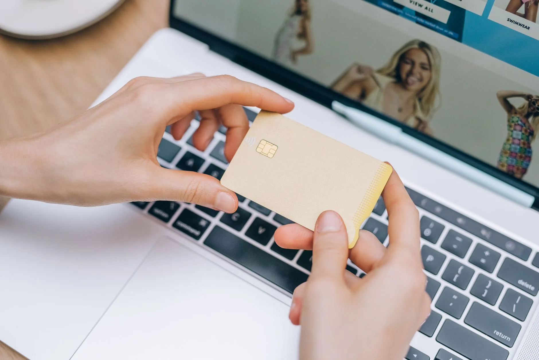 Osoba trzyma kartę kredytową nad klawiaturą laptopa