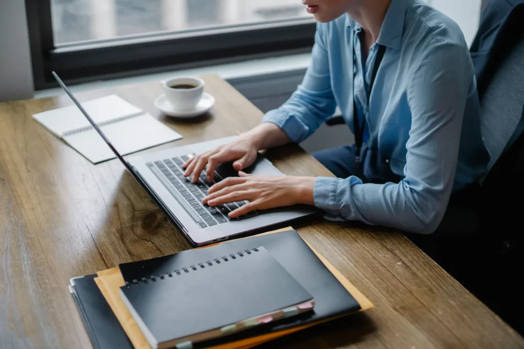 Osoba pisze na laptopie przy biurku z notatnikiem