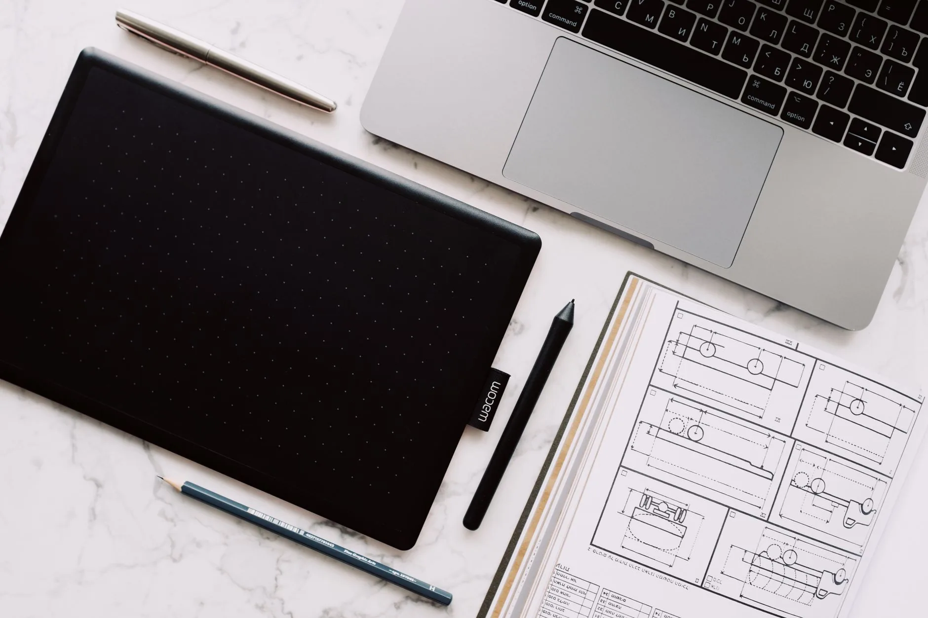 Na biurku leżą tablet graficzny, laptop i szkice